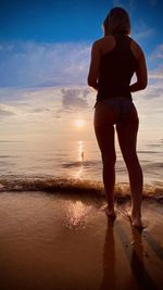 Rear view of woman standing on beach during sunset