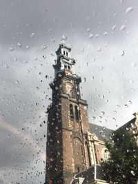 Low angle view of buildings seen through wet window