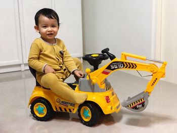 Portrait of smiling boy sitting in toy bulldozer on floor at home 