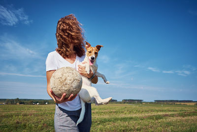 Woman holding dog with ball on field against sky