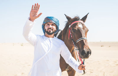Portrait of man with horse walking at desert against clear sky