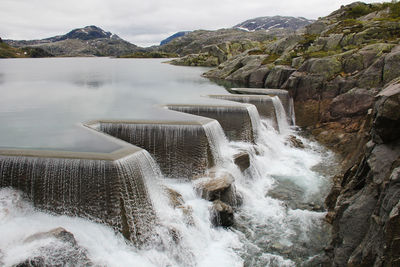 Scenic view of waterfall by mountains against sky