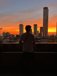 Rear view of man standing in city against sky during sunset