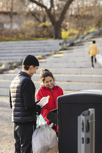 Smiling female and male volunteers throwing plastic waste in garbage can