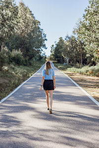 Rear view of woman walking on road against trees