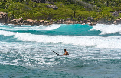 Man laying on surfboard on waves on turquoise ocean in idyllic tropical bay