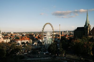 Illuminated ferris wheel in city against sky