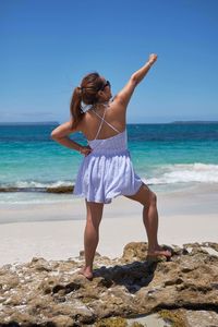 Rear view of mid adult woman standing at beach against clear blue sky