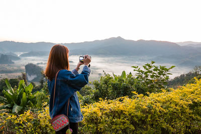 Man photographing with camera on mountain against sky