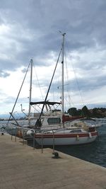 Sailboats moored at harbor against sky