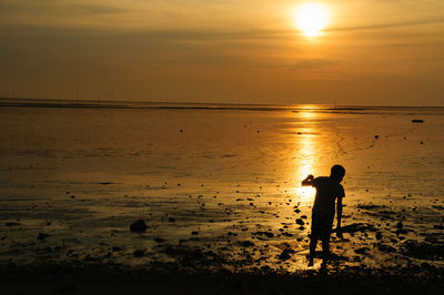 Silhouette man standing on beach against sky during sunset