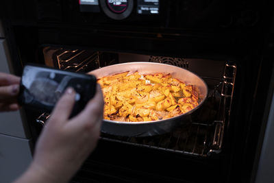A food blogger takes pictures with phone and shoots food in the oven that she has cooked. 