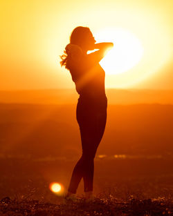 Silhouette woman standing against sun during sunset