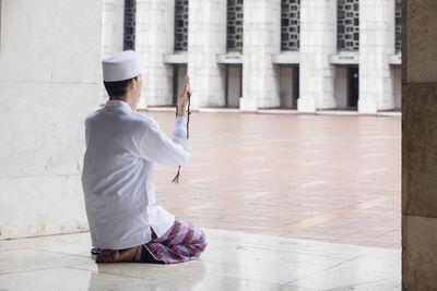 Man in traditional clothing with beaded necklace praying in corridor