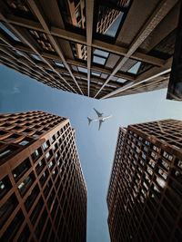 Low angle view of buildings against sky with a plane passing by