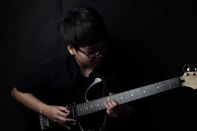 Boy playing guitar against black background