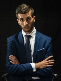 Portrait of young man in suit sitting against black background