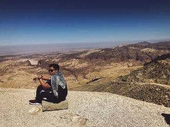 Full length of man sitting on rock against landscape