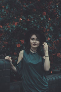 Beautiful young woman standing by retaining wall against flowering plant