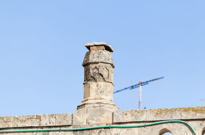 Low angle view of bird perching on a column against sky