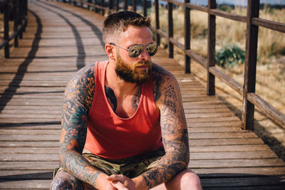 Young man wearing sunglasses while sitting on boardwalk