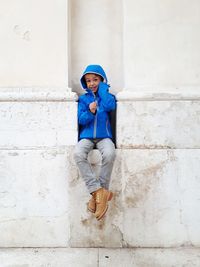 Portrait of boy sitting against wall