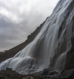 Low angle view of waterfall against cloudy sky