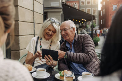 Happy senior couple sharing smart phone while sitting at sidewalk cafe