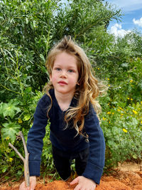 Portrait of young buy blond hair standing against plants