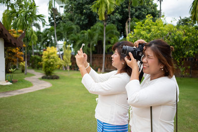 Young woman photographing with camera while standing by trees