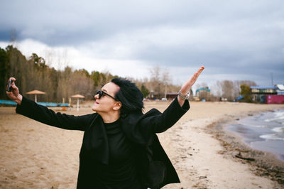 Woman taking selfie through mobile phone at beach against sky