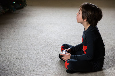 Side view of boy holding game controller while sitting at home