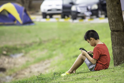 Boy using mobile phone on lawn in city