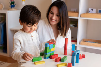 Mother assisting son in puzzle sitting at home