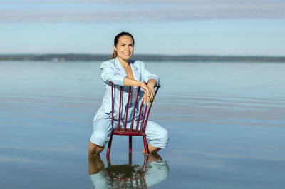Digital nomad woman, female business entrepreneur sits in chair in water, blue sky is on background