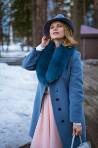 Beautiful woman in blue coat and hat posing outdoors in the snow