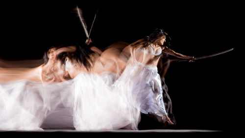 Blurred image of woman holding sword against black background