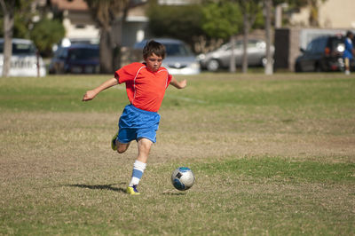 Young soccer player in red blue uniform kicking soccer ball in park