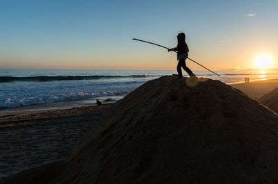 Silhouette man fishing at beach against sky during sunset