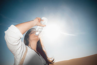 Low angle view of woman holding umbrella against sky on sunny day