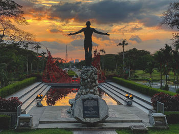 Statue of man in city against sky during sunset