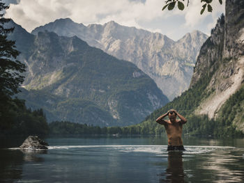 Shirtless man standing in lake against mountains