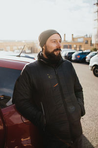 Young bearded man standing by car in city