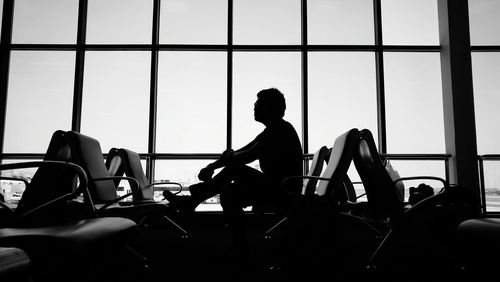 Silhouette man sitting against window at airport