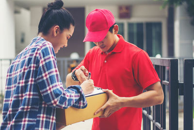 Female customer signing receipt while receiving package from delivery man at gate