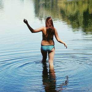 Rear view of woman wearing bikini walking in river