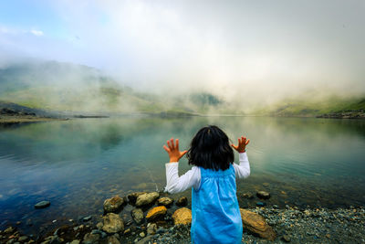 Girl standing at lakeshore during foggy weather