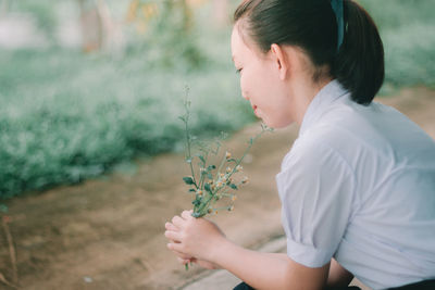 Side view of young woman holding flowers while sitting outdoors