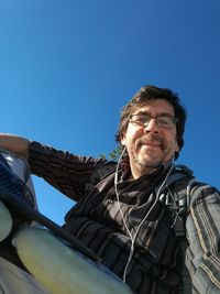 Low angle view of mature skater listening music through headphones against clear blue sky