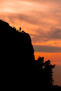 Silhouette people on rock against sky during sunset